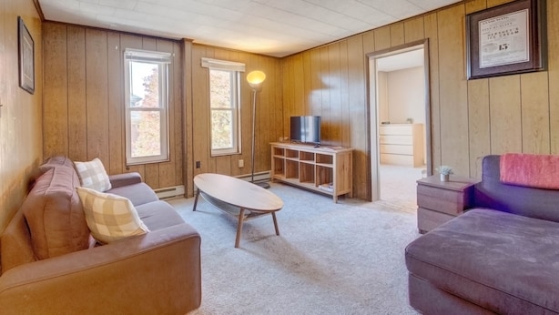 A cozy living room with wooden walls, a brown leather sofa, a small coffee table, and a television on a wooden stand.