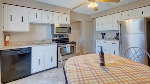 A modern kitchen with white cabinets, stainless steel appliances, and a ceiling fan.