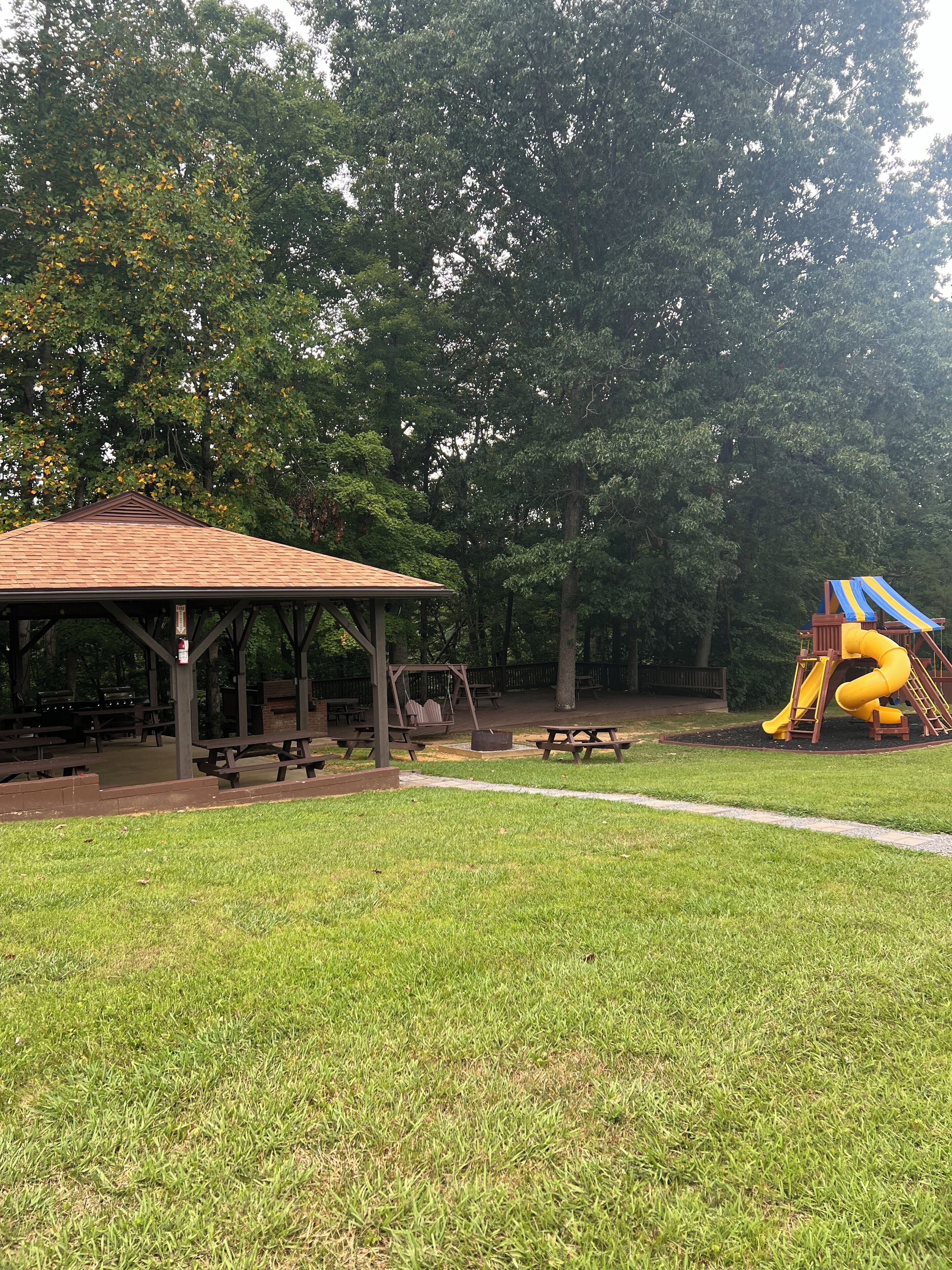 Ein Park mit Picknicktischen, einem überdachten Pavillon und einem Spielplatz mit einer gelben Rutsche.