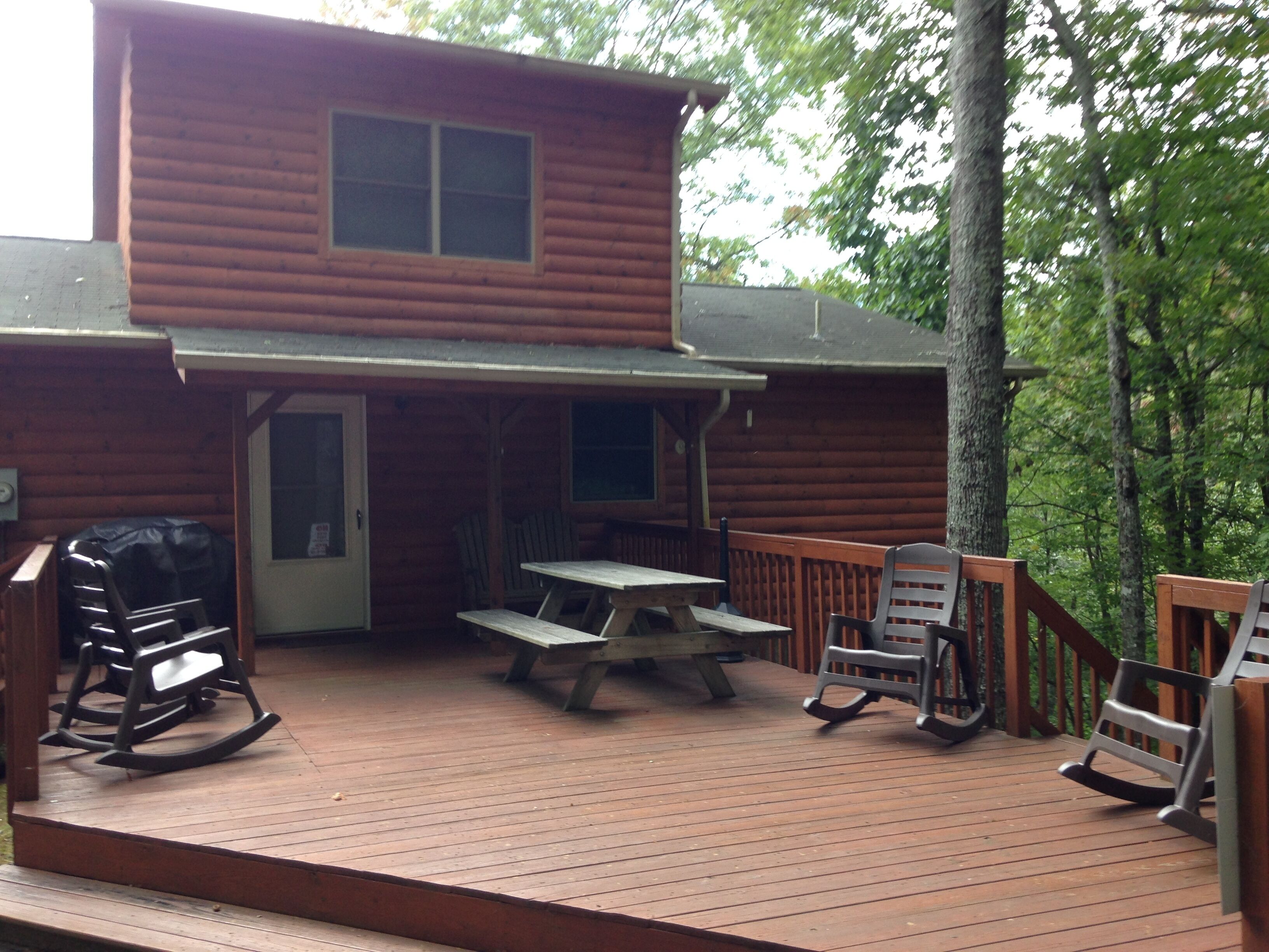 A wooden cabin with a deck, picnic table, and rocking chairs.
