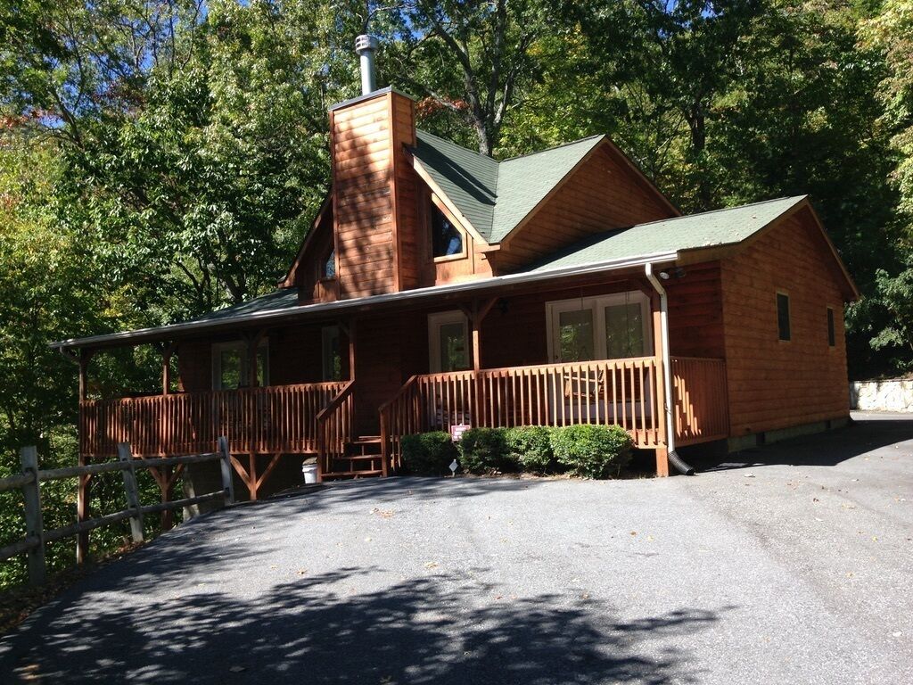 A wooden cabin with a porch, a chimney, and a fenced driveway.
