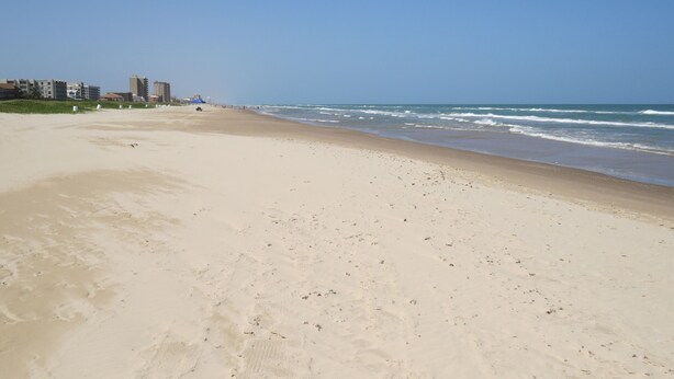 Een breed zandstrand met een helderblauwe lucht.
