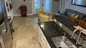 Een keuken met een granieten aanrecht, een roestvrijstalen spoelbak en een eethoek met een grijze bank en een gele fauteuil.