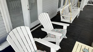 Een veranda met witte Adirondack-stoelen en een kleine tafel.