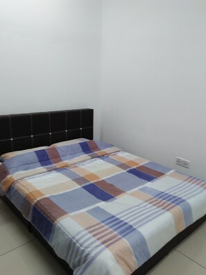 Una cama con colcha escocesa en una habitación con pared blanca lisa y cabecera negra.