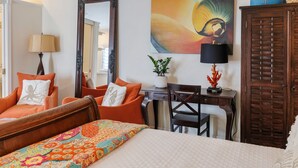 A hotel room with a bed, orange armchair, desk, and a large mirror. - Studio Blu - Historic Key West Studio + Bikes (Key West)