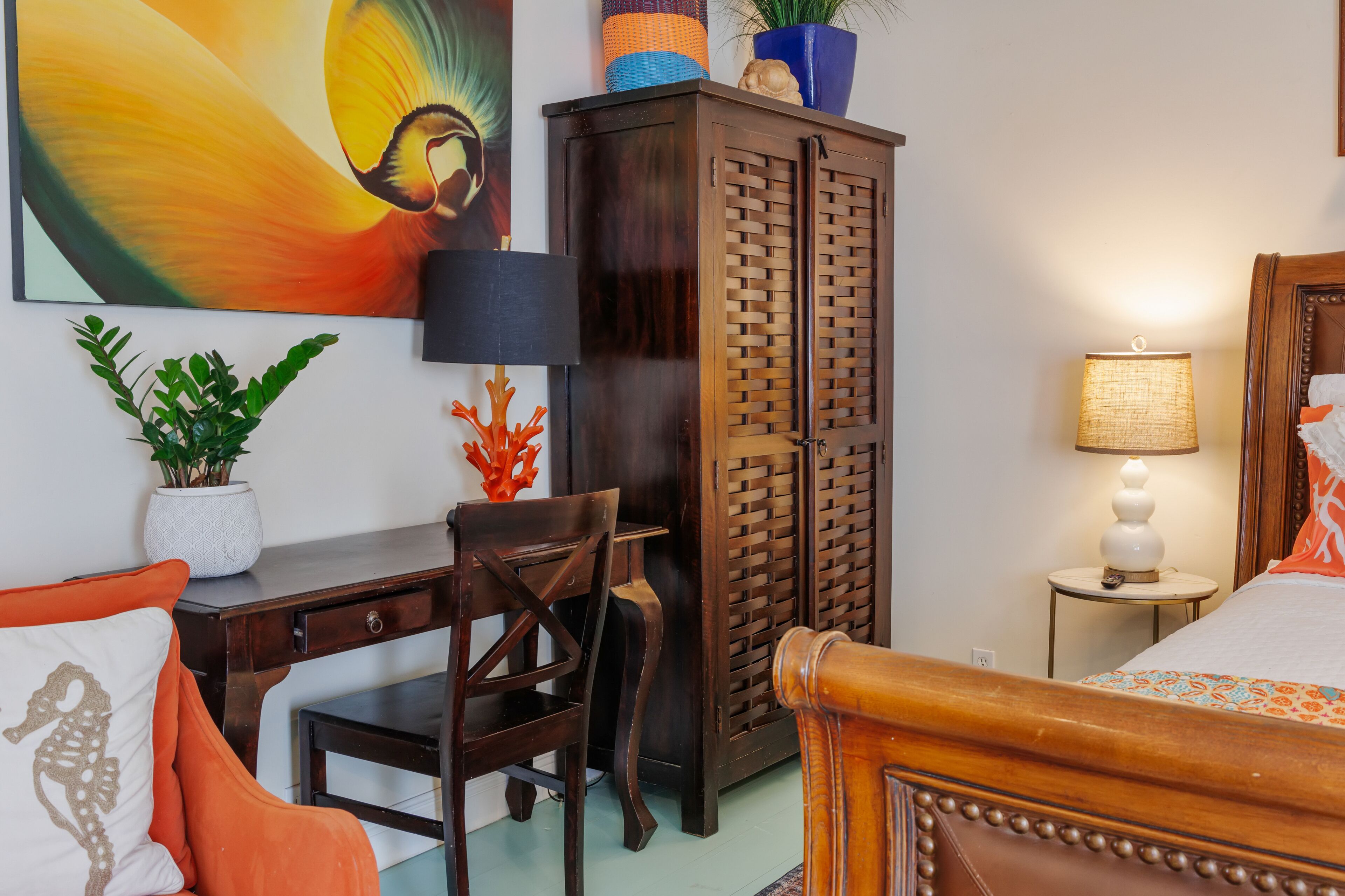 A bedroom with a wooden bed, a desk, a chair, a wardrobe, and a nightstand with a lamp.