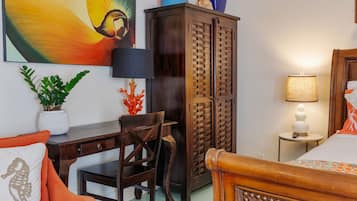 A bedroom with a wooden bed, a desk, a chair, a wardrobe, and a nightstand with a lamp.