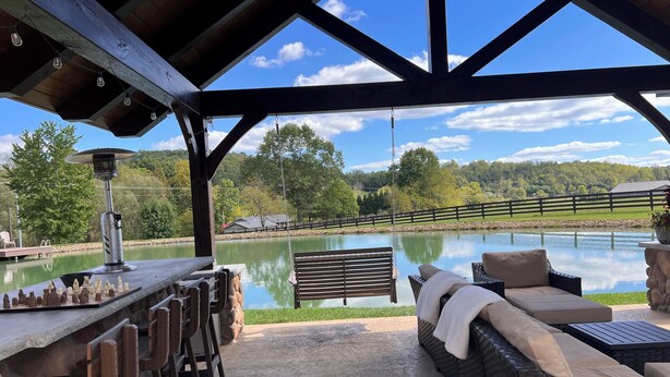 A covered outdoor seating area with a view of a lake, a swing, and a bar with chess pieces.