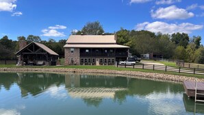 A lodge with a stone exterior, a large deck, and a pond in front.