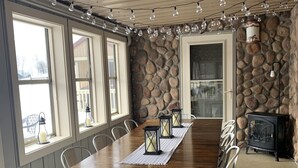 A dining area with a wooden table, white chairs, stone walls, and a stone fireplace.