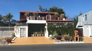 Una casa de dos pisos con techo de tejas rojas, una reja en la entrada y un camino de acceso pavimentado.