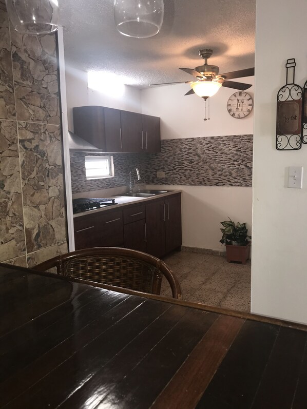 A compact kitchen with dark wooden cabinets, a stone backsplash, and a ceiling fan. - Ponce holiday apartment (Ponce)