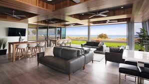 Ein modernes Wohnzimmer mit Meerblick, ausgestattet mit einer Couch, Sesseln, einem Essbereich und Deckenventilatoren.