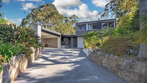 A modern house with a covered driveway, stone walls, and lush greenery. - Treehouse, Vincentia - 5 min walk to the beach (Vincentia)