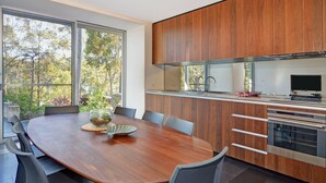 A modern kitchen with wooden cabinets, a built-in oven, and a large window overlooking a garden. - Treehouse, Vincentia - 5 min walk to the beach (Vincentia)