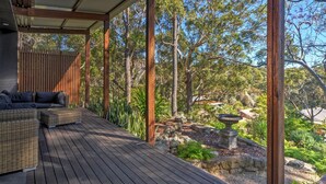 A covered outdoor area with a wooden deck, wicker furniture, and a stone fountain. - Treehouse, Vincentia - 5 min walk to the beach (Vincentia)