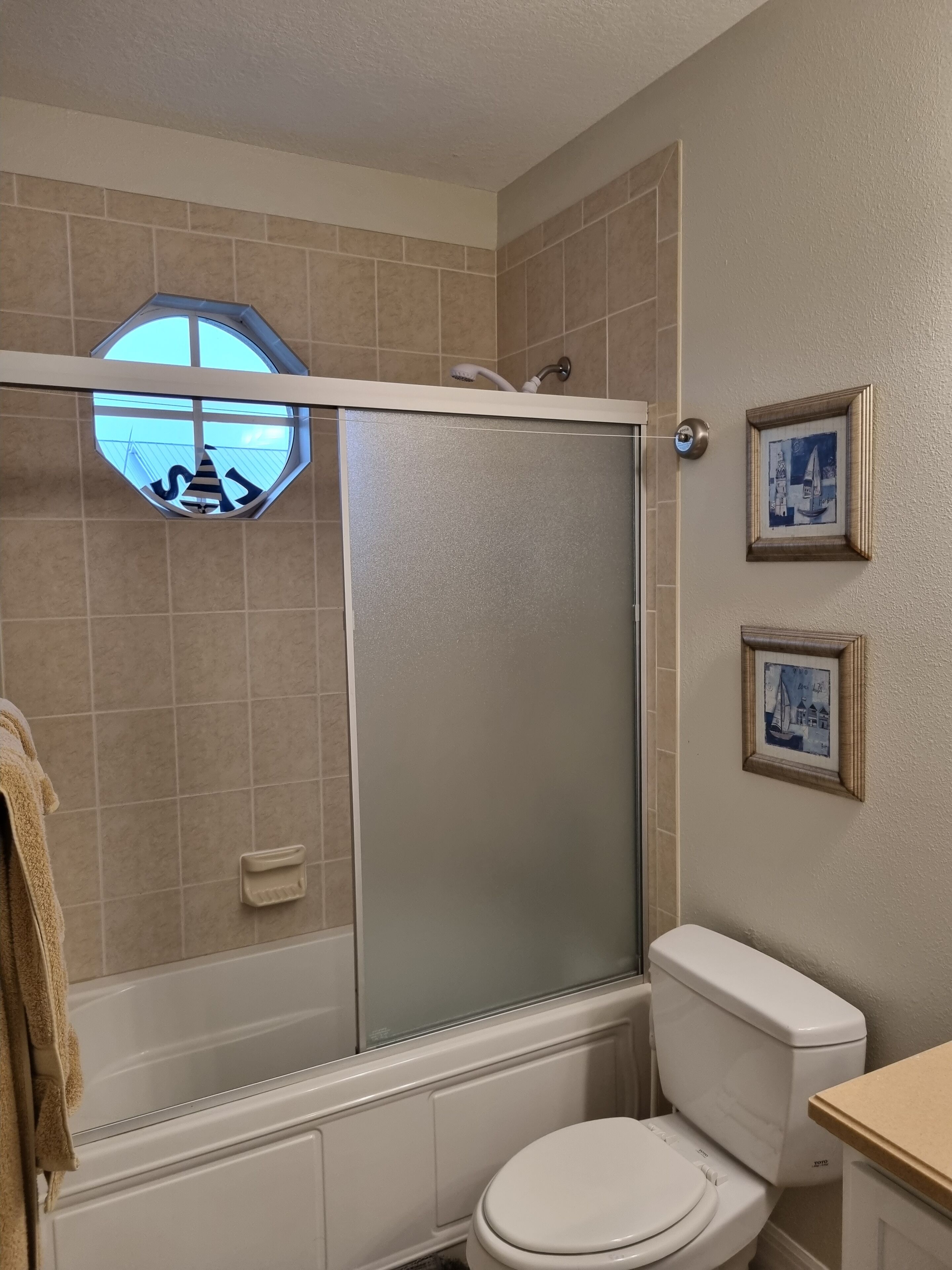 A bathroom with a shower enclosure, toilet, and two framed pictures on the wall.