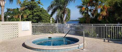 En swimmingpool med kakelbeklädd kant, omgiven av ett vitt staket, palmer och en fri utsikt över havet.