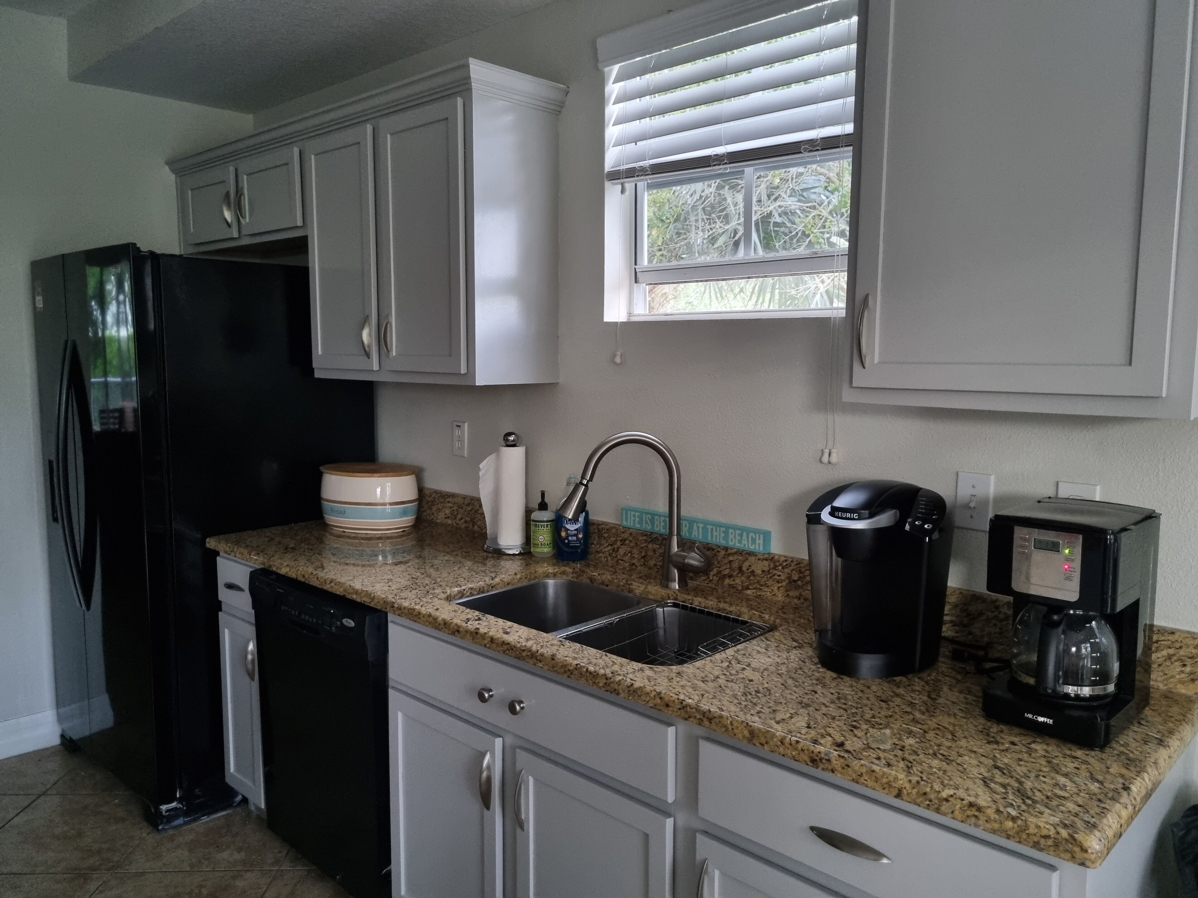 A kitchen with white cabinets, a black refrigerator, a coffee maker, and a sink.