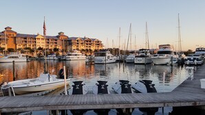 Un port esportiu amb diverses embarcacions amarrades, un moll de fusta i un edifici d'hotel de diversos pisos al fons.