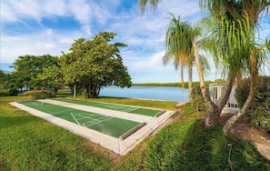 Un campo da croquet con una distesa d'acqua sullo sfondo, circondato da vegetazione lussureggiante e palme.