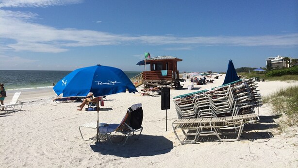 Een strand met ligbedden, parasols en een bewakingstoren.