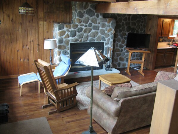 A cozy living room with a stone fireplace, wooden furniture, and a television.
