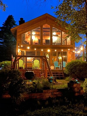 A two-story wooden cabin with a porch, multiple windows, and outdoor seating.