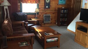 Un salon chaleureux avec un plafond en bois, une cheminée, un canapé, une table basse, une bibliothèque et un téléviseur.