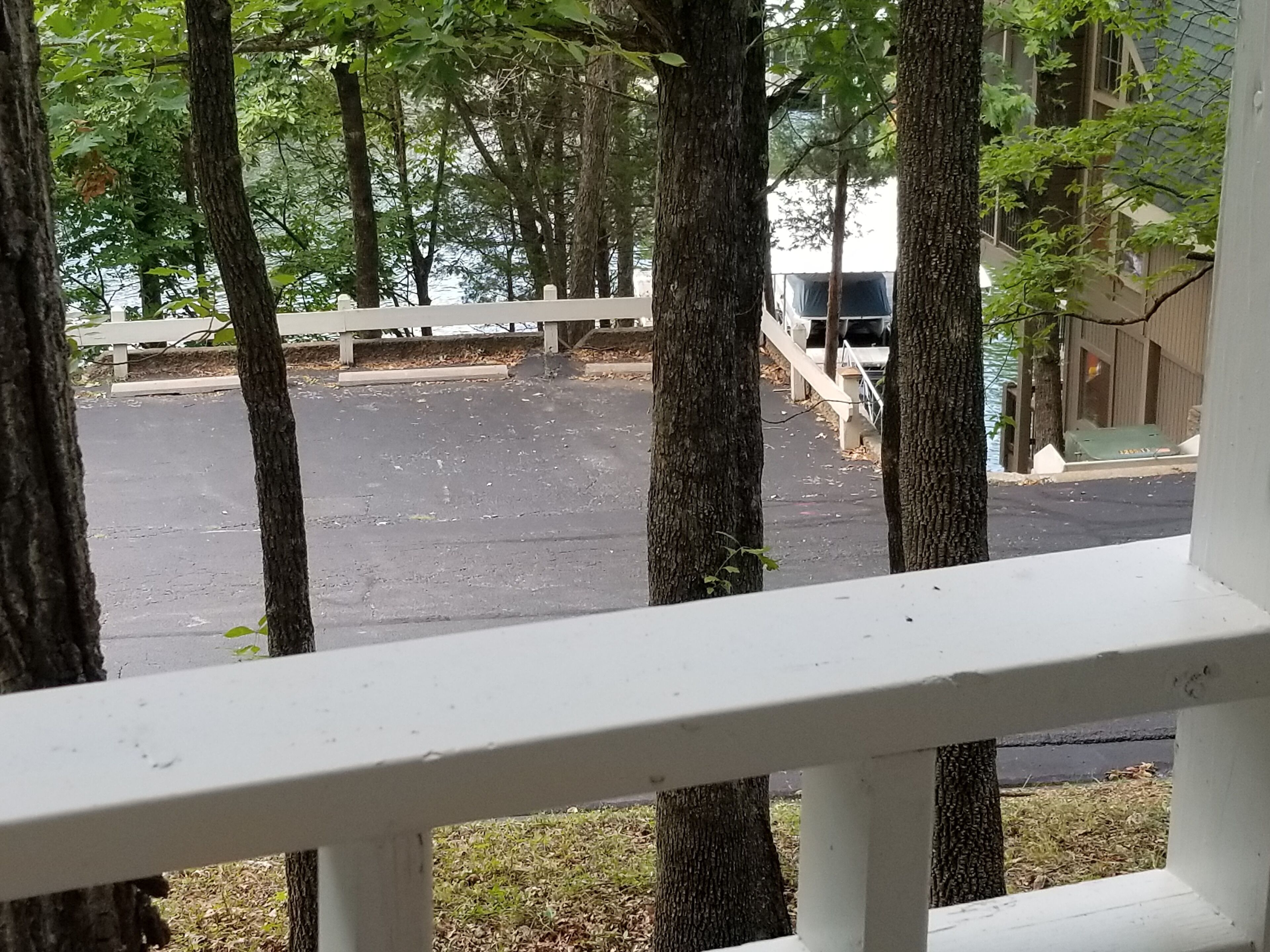 Blick von einer Veranda mit weißer Reling auf einen Parkplatz, Bäume und ein Gebäude im Hintergrund.