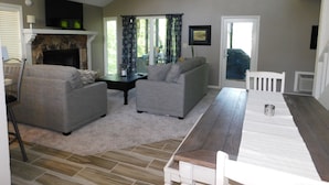 A living room with a fireplace, two sofas, a dining table, and a ceiling fan.