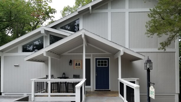 A two-story building with a covered porch, a blue door, and a small outdoor seating area with a table and chairs.