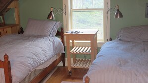 Two single beds with wooden frames and striped bedding, a small wooden nightstand with a lamp, and a window with a view of greenery.