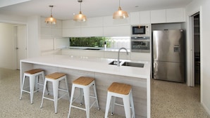 A modern kitchen with a central island, stainless steel appliances, and three bar stools. - SALT - Luxury Oceanside Oasis (West Busselton)