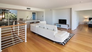 A modern living room with a white sofa, a TV, and a staircase leading to an upper level. - SALT - Luxury Oceanside Oasis (West Busselton)