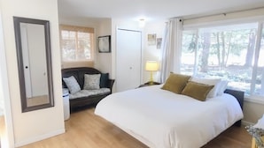 Une chambre à coucher avec un grand lit, un canapé, une fenêtre avec des rideaux et une bouche d’aération au plafond.