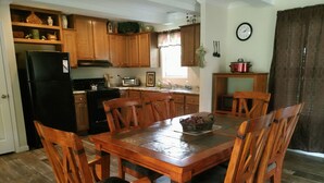 Una mesa de comedor de madera con seis sillas, un refrigerador negro, armarios de madera, un microondas, una estufa y un reloj en la pared.