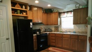 Una cocina con armarios de madera, un refrigerador negro, una estufa y una ventana con cortina.