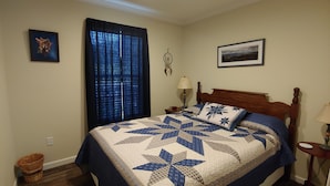 Un dormitorio con una cama grande, una ventana con cortinas, un atrapasueños colgado en la pared y un cuadro enmarcado sobre la cama.