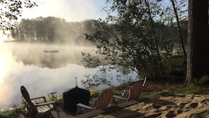 Et siddeområde ved søen med grill, stole og en sti med sand.