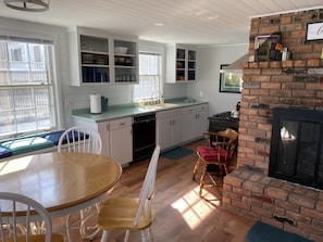 A kitchen with white cabinets, a brick fireplace, and a dining area with a wooden table and chairs.