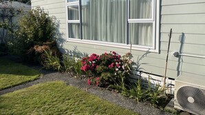 Een huis met een groot raam, een kleine tuin met bloemen en een airconditioning.