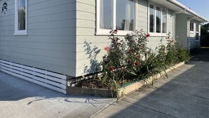 Een gelijkvloers huis met een veranda, een kleine tuin met bloemen en een heldere lucht.