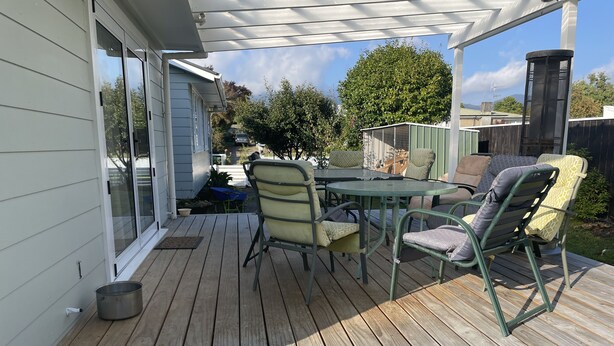 Een overdekt terras met een houten terras, een metalen tafel en stoelen.