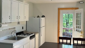 A kitchen with white cabinets, a stove, a sink, and a refrigerator. There is a dining table with chairs and a door leading outside. - Romantic getaway, private cabin overlooking Sawyer Lake  WIFI, TV, AC, Heat (Gilmanton)