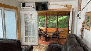 A cabin interior with a wooden deck, a television mounted above a door, and a fishing rod. - Romantic getaway, private cabin overlooking Sawyer Lake  WIFI, TV, AC, Heat (Gilmanton)