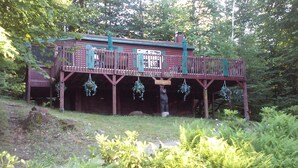 A wooden cabin with a balcony, surrounded by greenery. - Romantic getaway, private cabin overlooking Sawyer Lake  WIFI, TV, AC, Heat (Gilmanton)