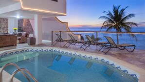 Un espace piscine avec des chaises longues et une vue sur l’océan au coucher du soleil.