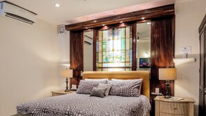 Une chambre à coucher comprenant un lit, des tables de chevet, un ventilateur de plafond, un appareil de climatisation et une fenêtre à vitraux.